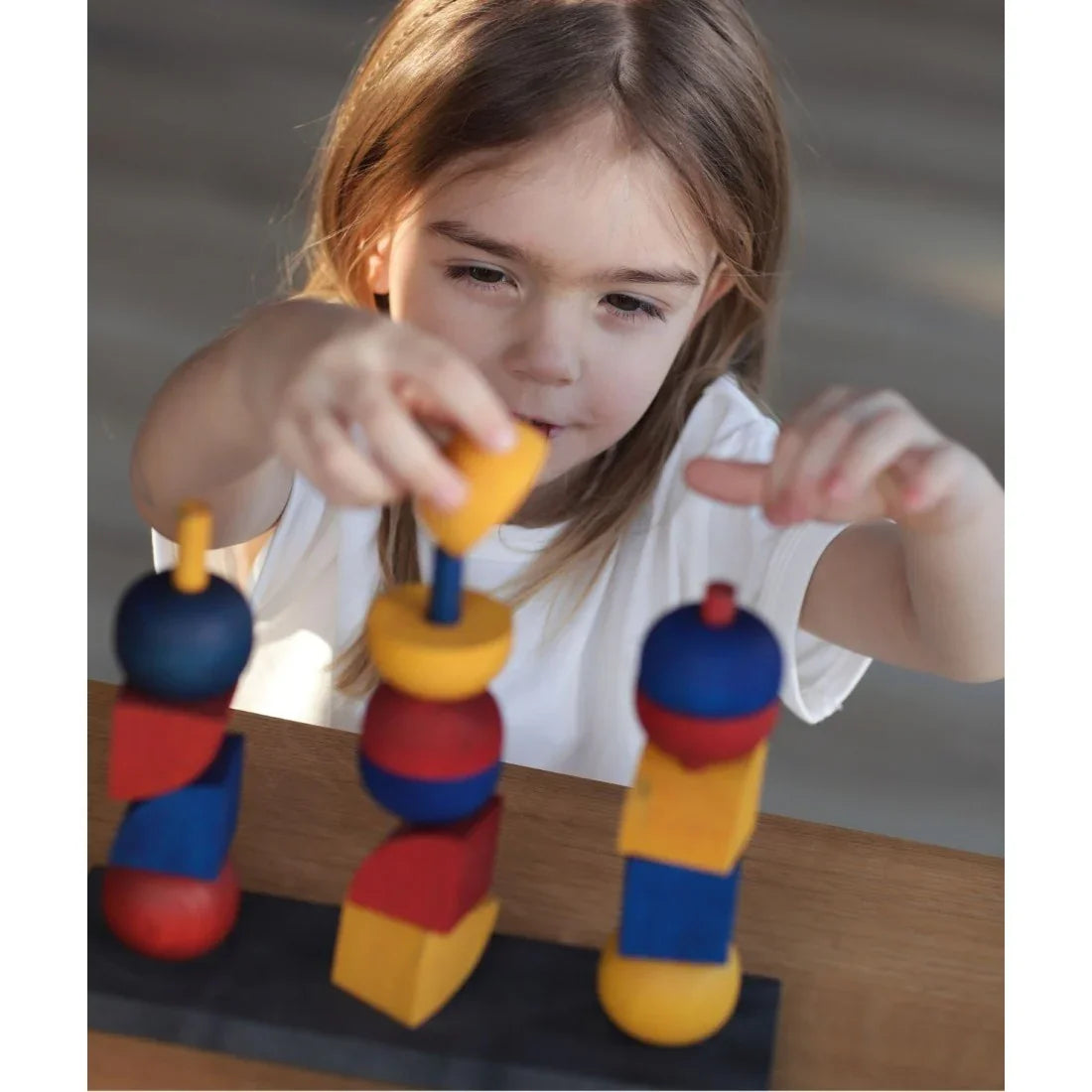 Child playing with a colorful wooden stacking toy, supporting Montessori-inspired learning, hand-eye coordination, creativity and screen-free play.