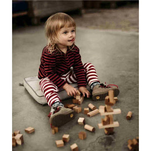 Toddler playing with natural wood building blocks on concrete floor, wearing striped red and white outfit