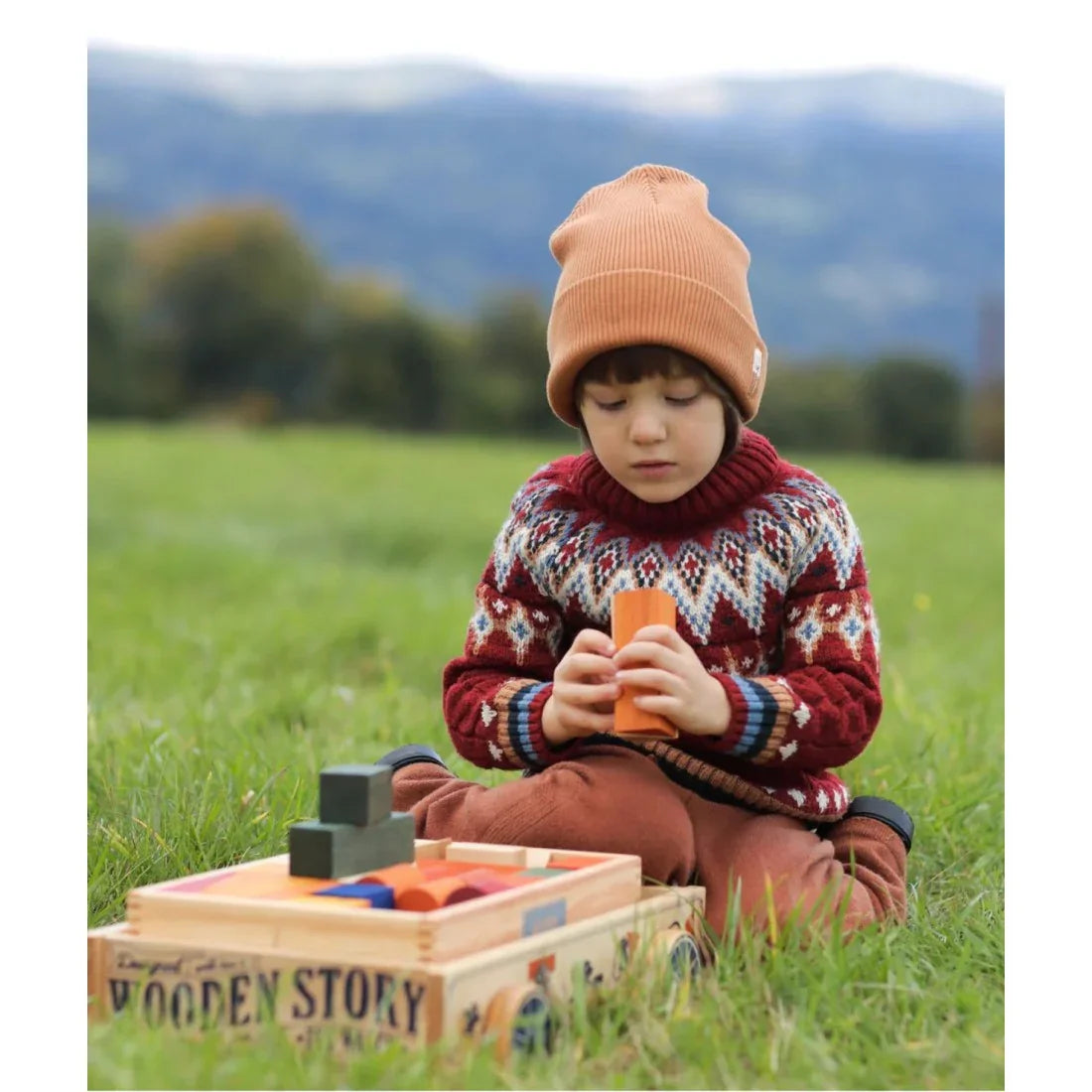 Child playing with colorful wooden blocks outdoors, supporting Montessori-inspired learning, creativity, fine motor skills and screen-free play.