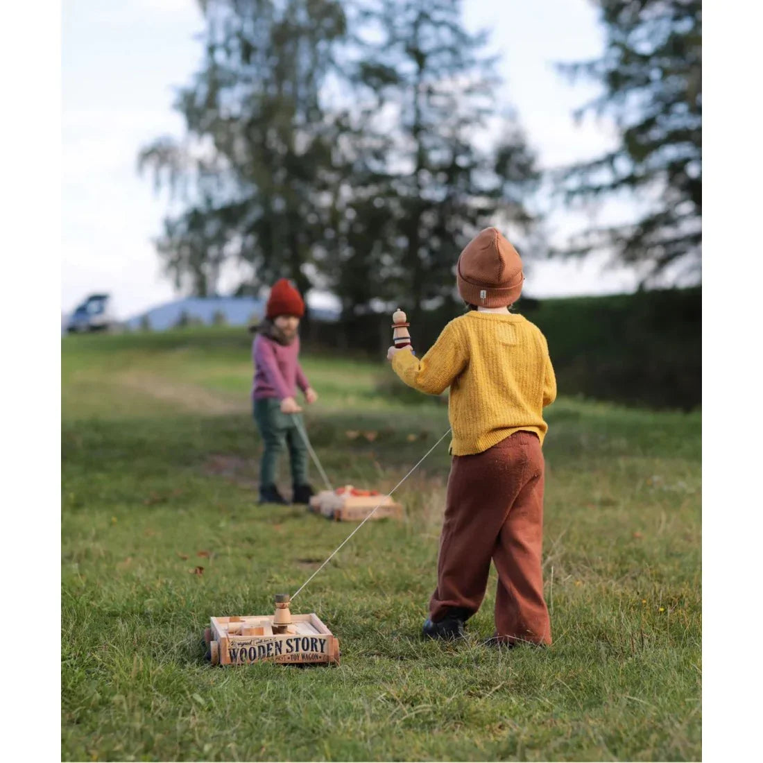 Children playing outdoors with a wooden toy wagon and natural blocks, encouraging screen-free imaginative play, movement and social development.