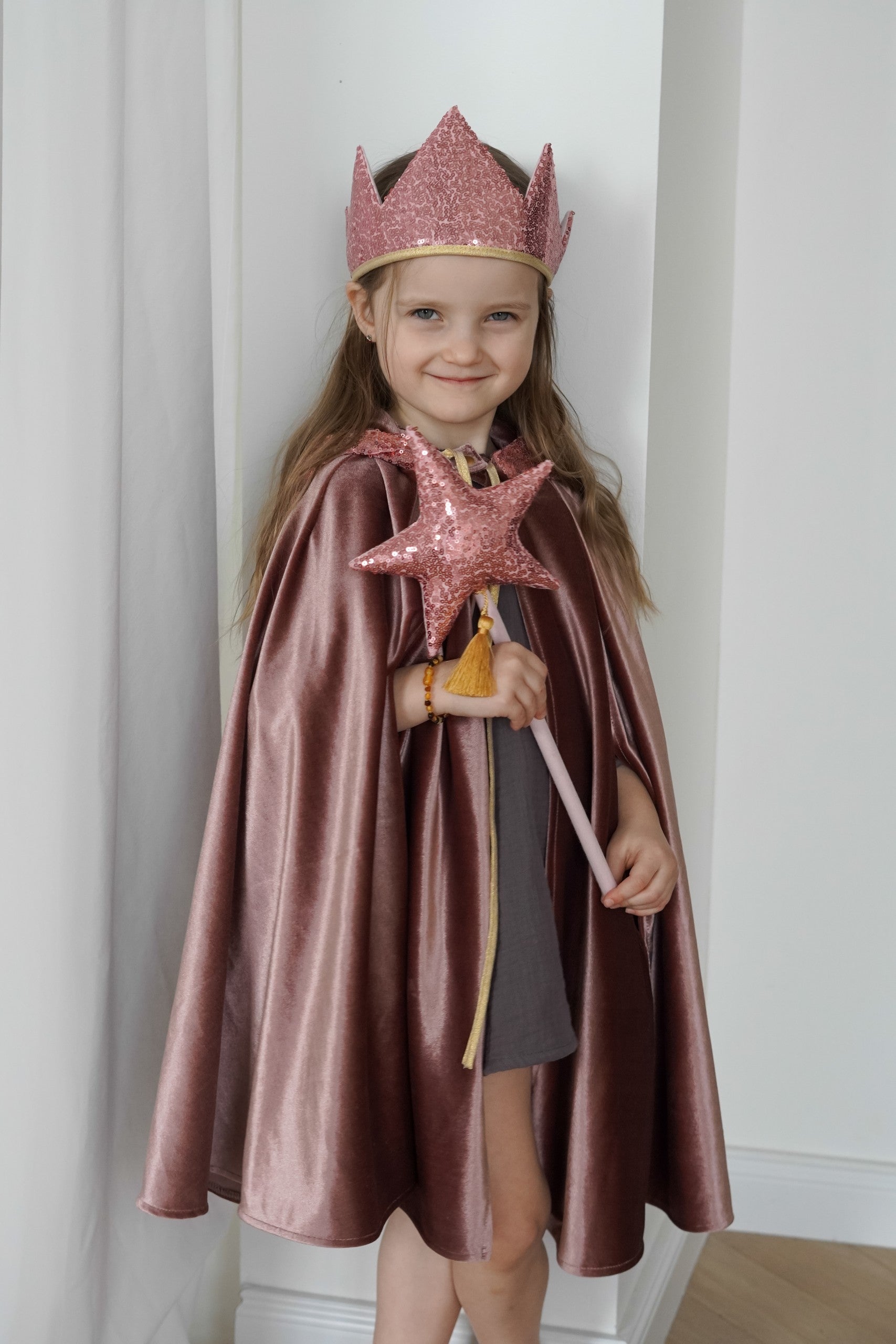 Child wearing the Cosmic Pearl magic cape with a pink crown and star wand during indoor dress-up play