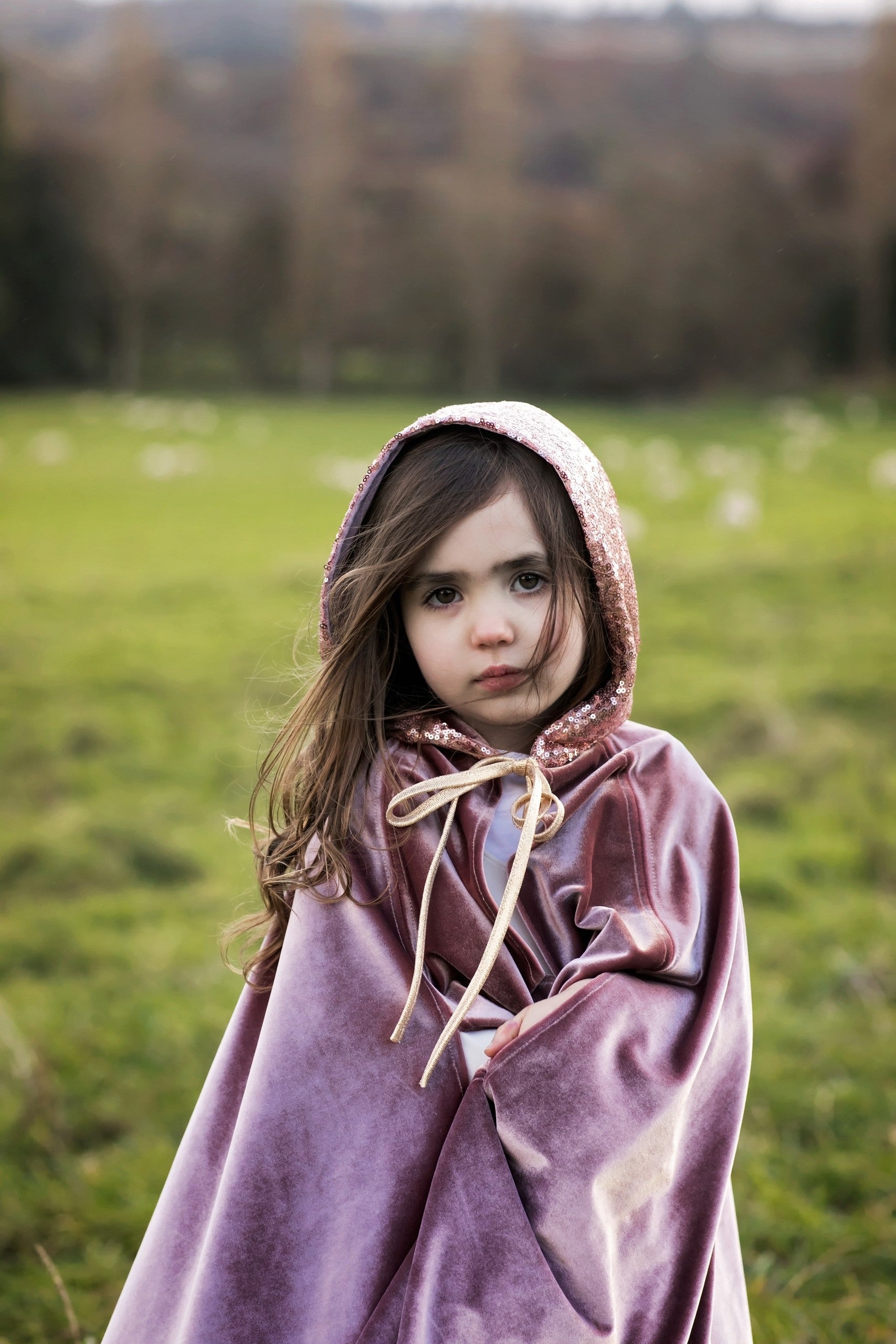 Close-up outdoor portrait of a child wearing the shimmering Cosmic Pearl cape with gold neck ties