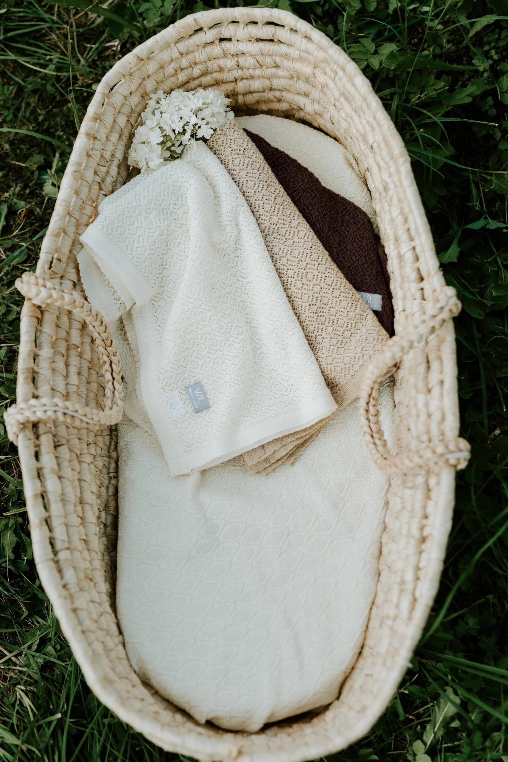 Couvertures bébé en tricot crème et beige avec motif texturé dans un panier en osier sur l'herbe