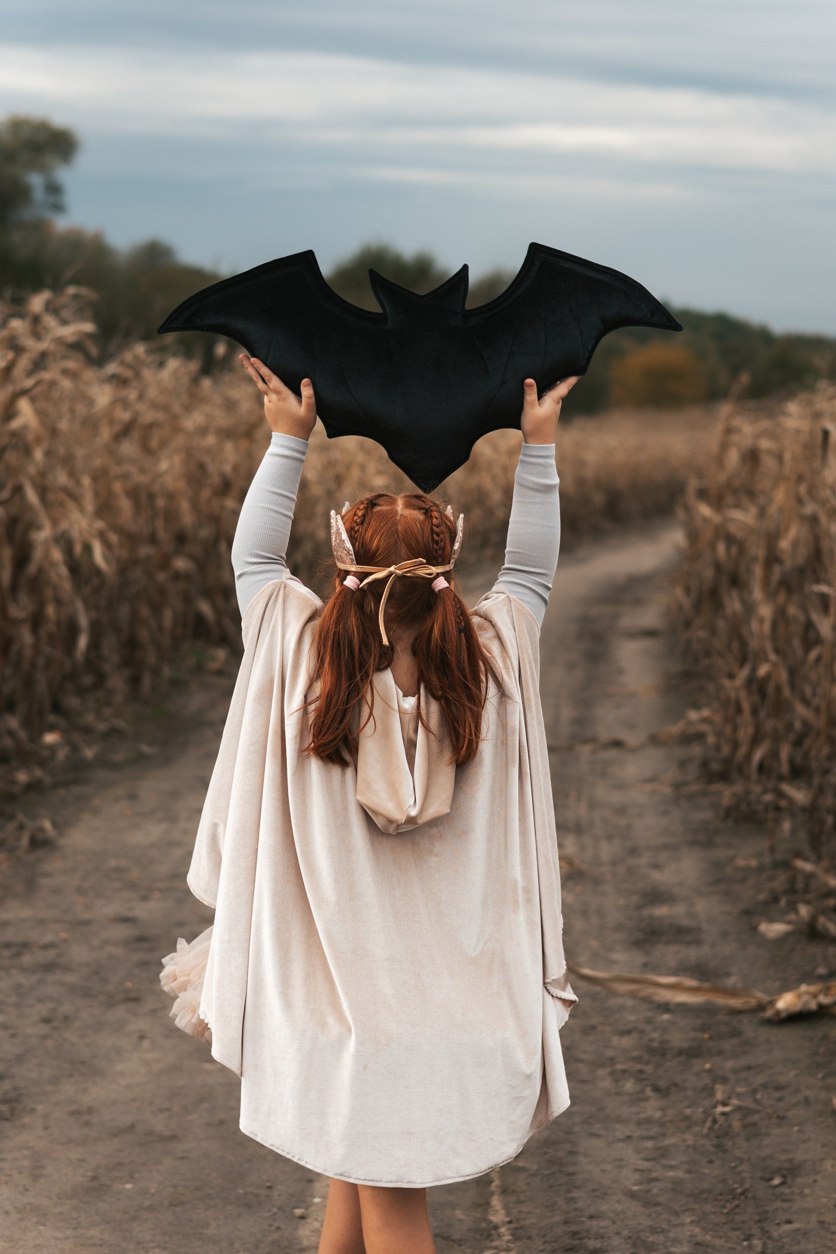 Back view of the Cream Pearl hooded cape as a child holds a large black bat decoration