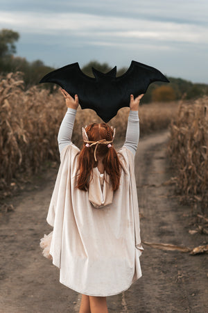 Back view of the Cream Pearl hooded cape as a child holds a large black bat decoration