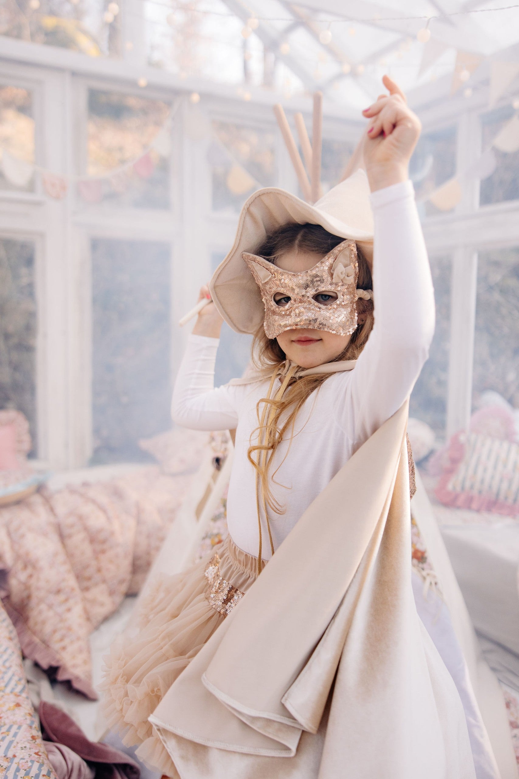 Child wearing a Cream Pearl hooded cape with a sequined cat mask during indoor dress-up play