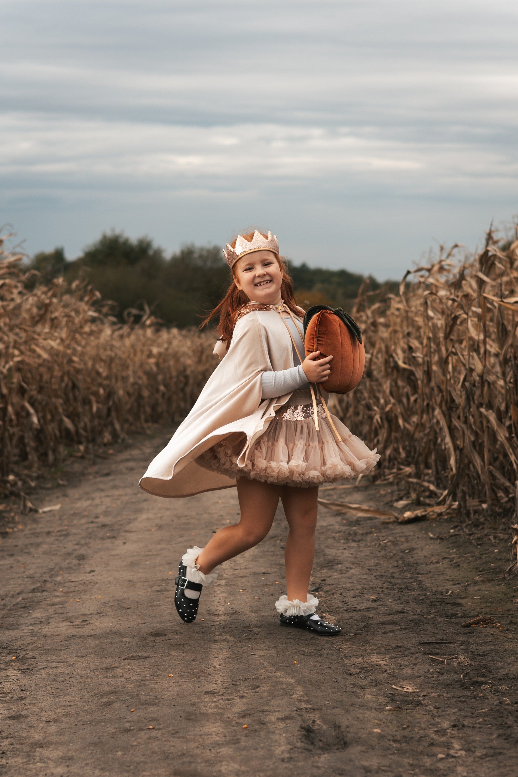 Child wearing the Cream Pearl magic cape and sparkling crown while carrying a velvet pumpkin outdoors