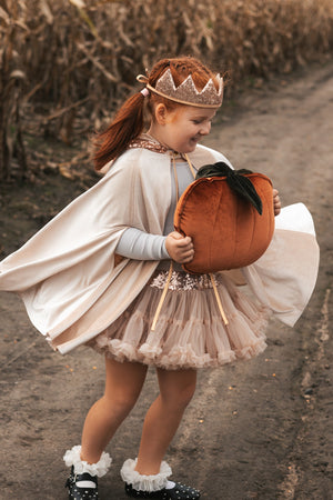 Child wearing the flowing Cream Pearl cape and holding an orange velvet pumpkin