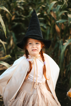 Child wearing the Cream Pearl cape with a tall black witch hat during outdoor fantasy play