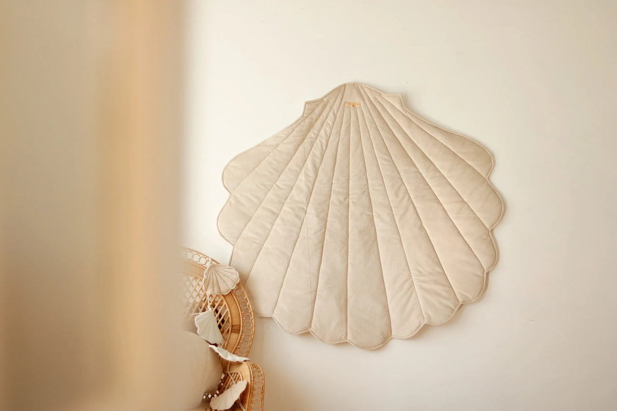 Cream Moi Mili shell playmat displayed as wall décor above a natural rattan chair in a neutral children’s room