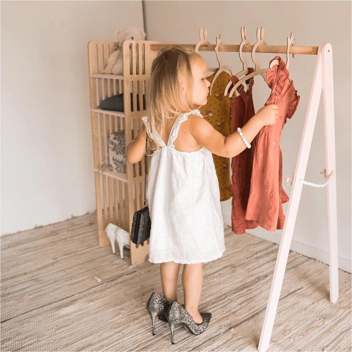 Child choosing a dress from white Ewart Woods Kids Wooden Clothing Rack with natural wooden hanging rail
