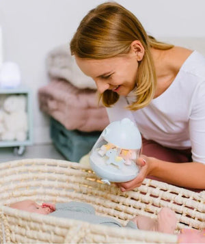 Mutter hält mobiles Pastell-Nachtlicht über das Baby in einer Wiege