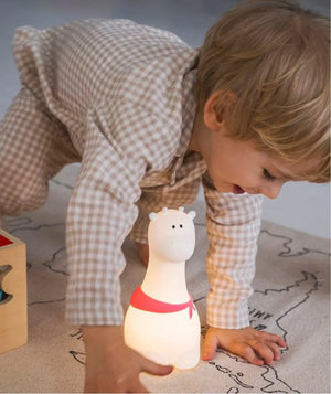 Enfant jouant avec une veilleuse girafe blanche ornée d'une écharpe rouge