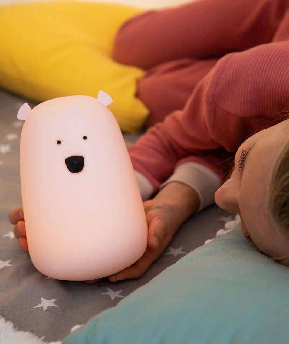 Bear-shaped nursery night light in soft white silicone, child holding on star-patterned bedding