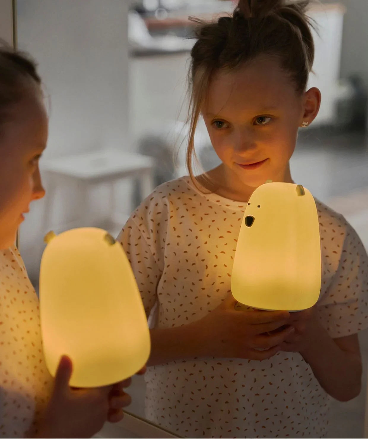 child holding bear-shaped yellow nursery night light in front of mirror
