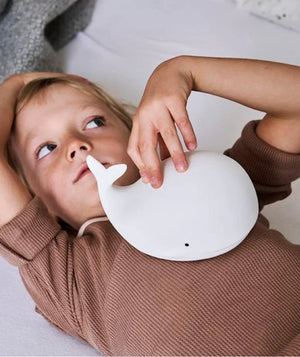 Enfant tenant une veilleuse baleine en silicone blanc dans une chambre chaleureuse