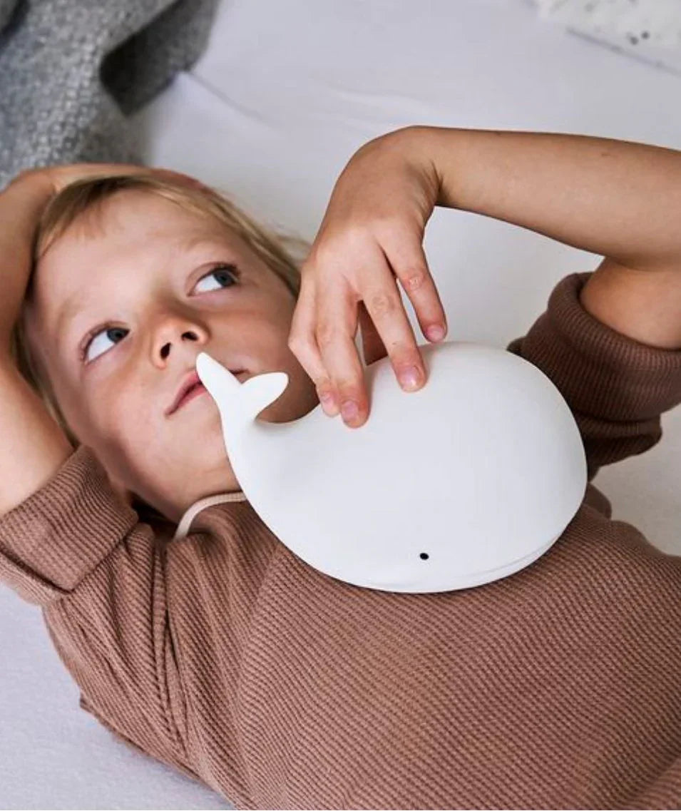 Enfant tenant une veilleuse baleine en silicone blanc dans une chambre chaleureuse