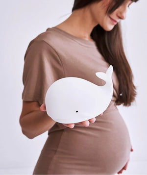 Veilleuse baleine en silicone blanc tenue par une femme en robe taupe