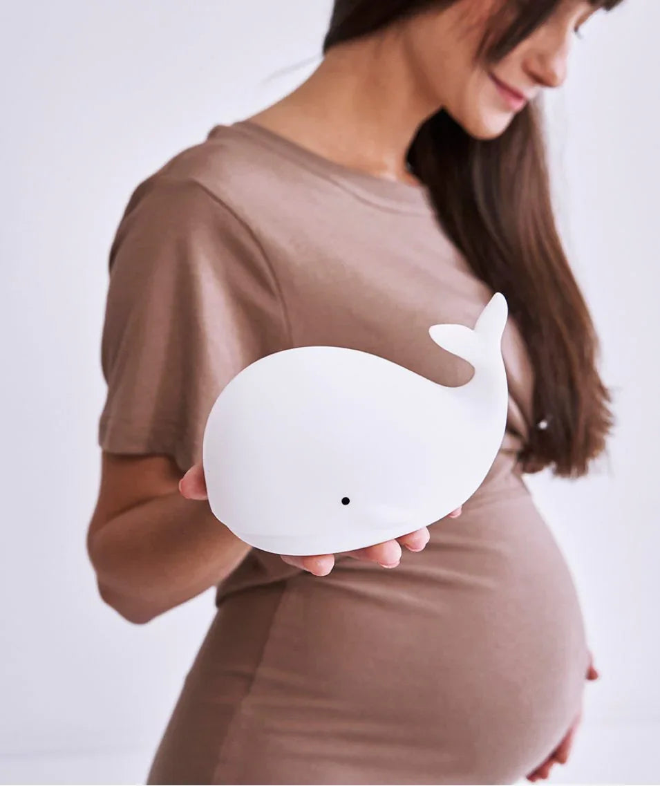 white whale-shaped silicone nursery night light held by woman in taupe dress