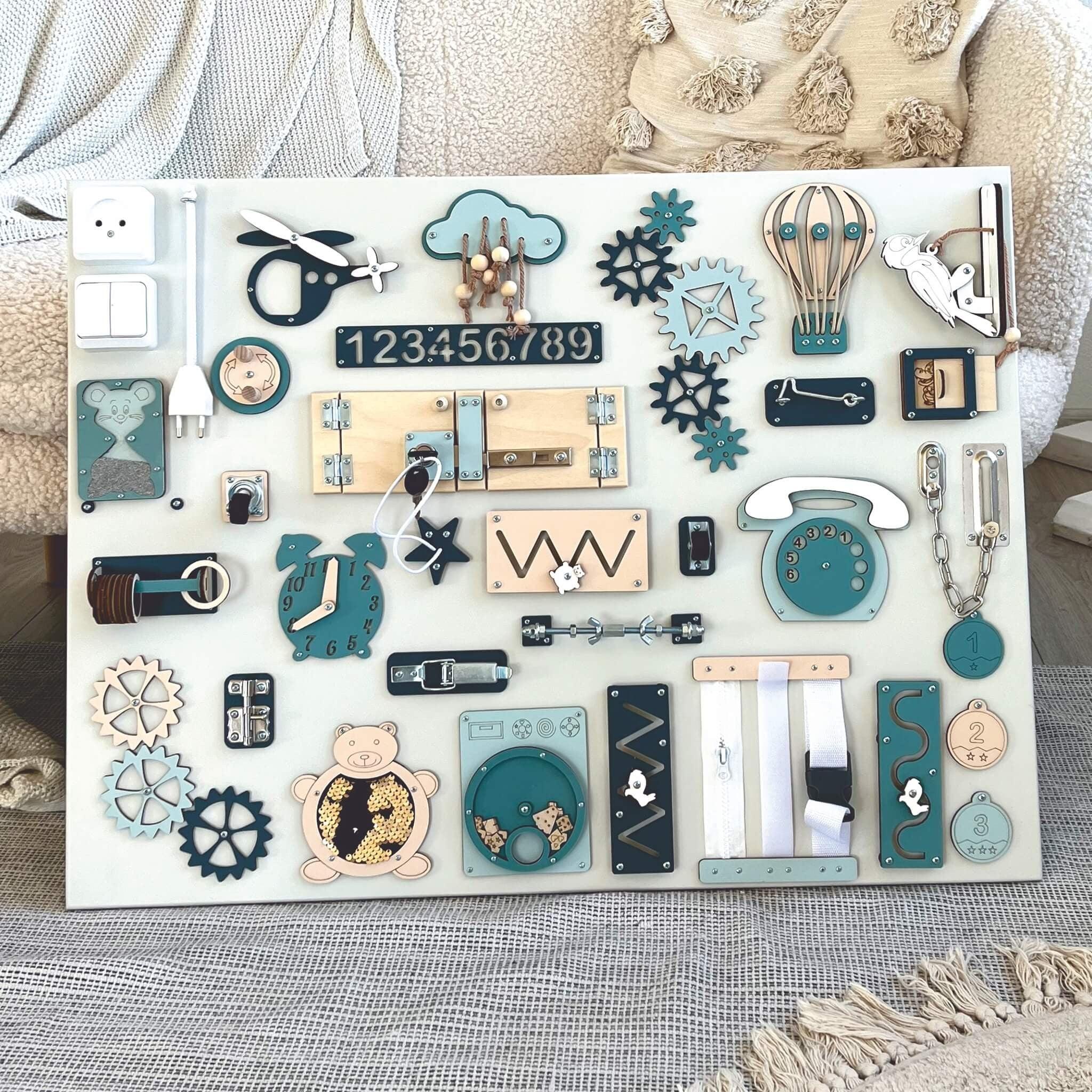Wooden Montessori busy board with teal, navy, and natural wood elements, featuring gears, latches, zippers, and number tiles for toddler fine motor skills.