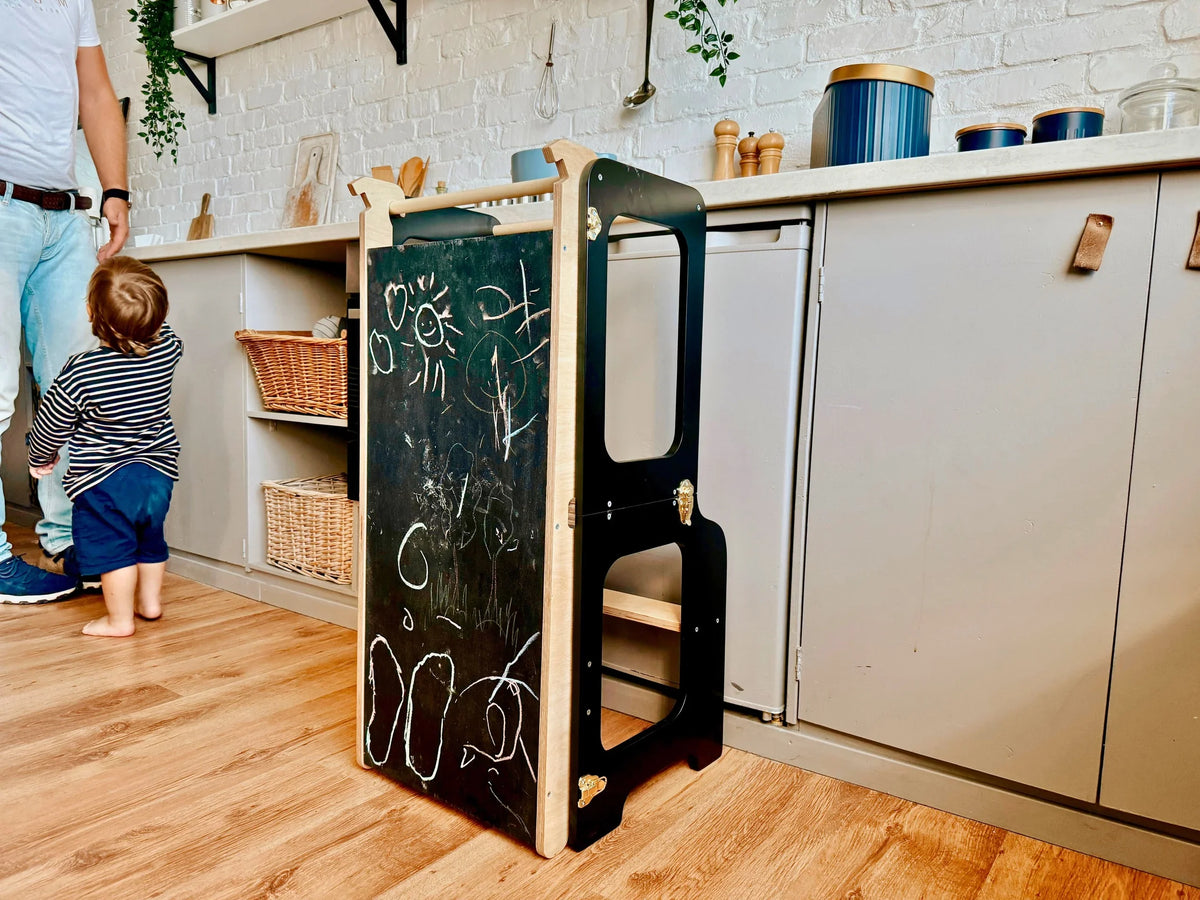 Black FAMILY Creative Learning Tower with chalk drawings on built-in blackboard beside kitchen counter