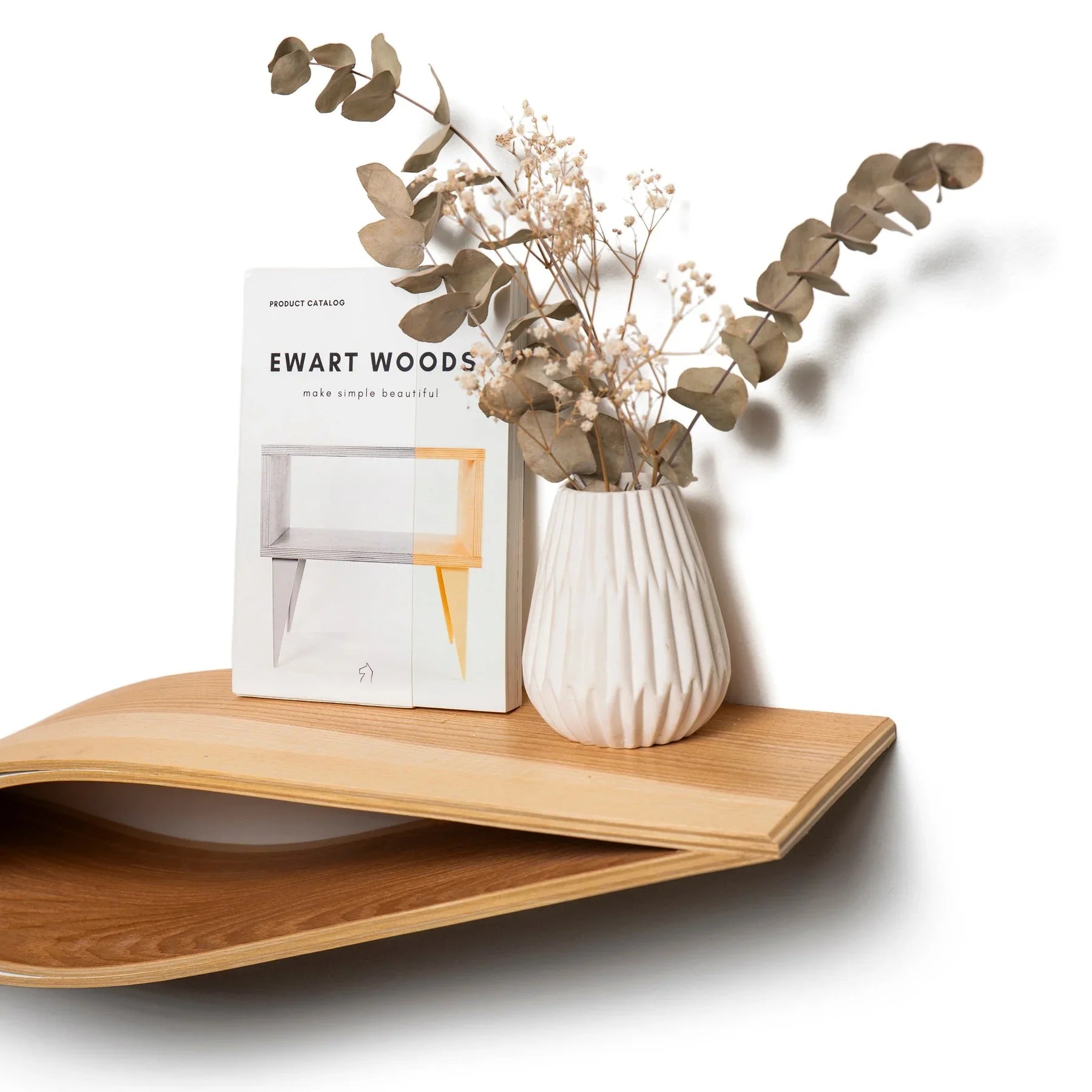 Mensola fluttuante da parete in legno con design curvato, che ospita un vaso bianco a coste e fiori secchi