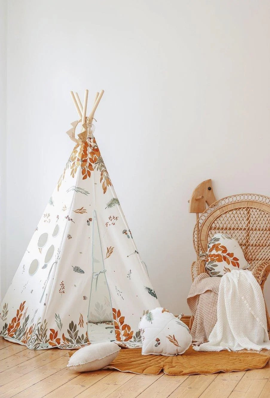 Forest Friends teepee styled beside a rattan chair with woodland cushions and a rust-coloured quilted mat