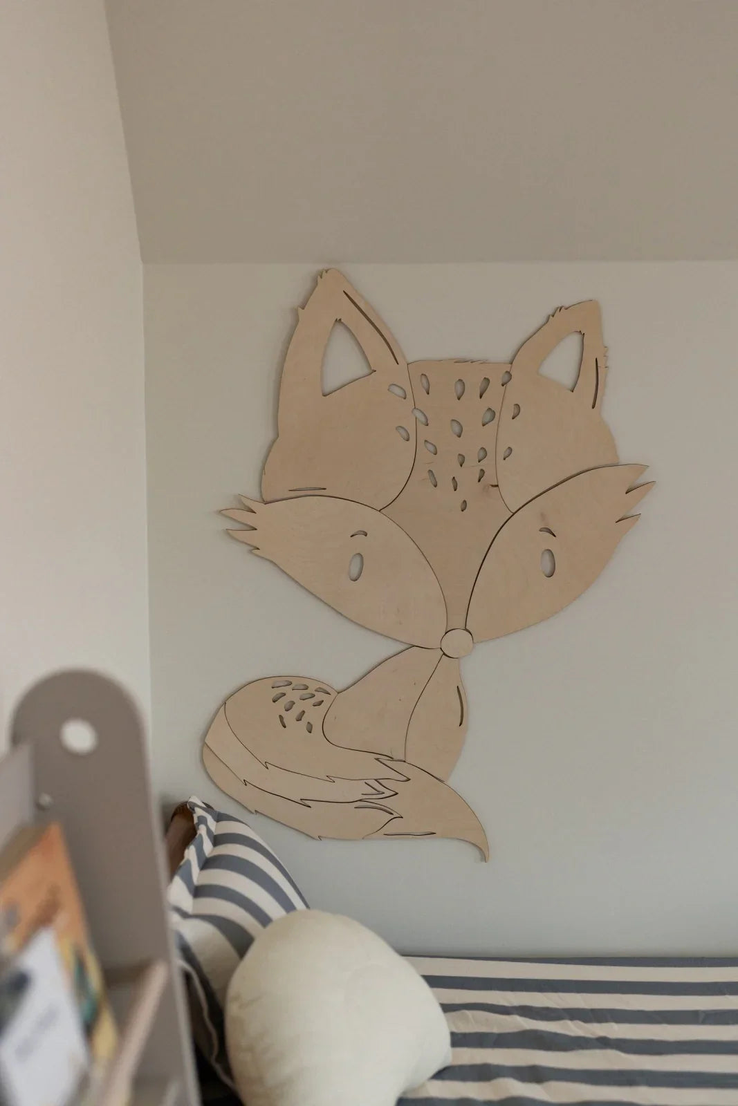 Decorazione da parete in legno a forma di volpe in una stanza per bambini minimalista sopra biancheria da letto a righe