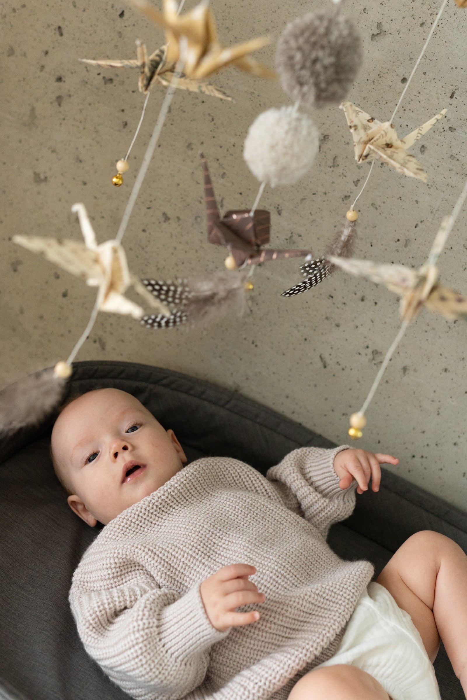 Close-up of a baby beneath the moving origami cranes, feathers and pompoms