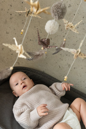 Close-up of a baby beneath the moving origami cranes, feathers and pompoms