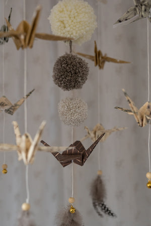 Close-up of cream, grey and brown yarn pompoms with folded paper cranes