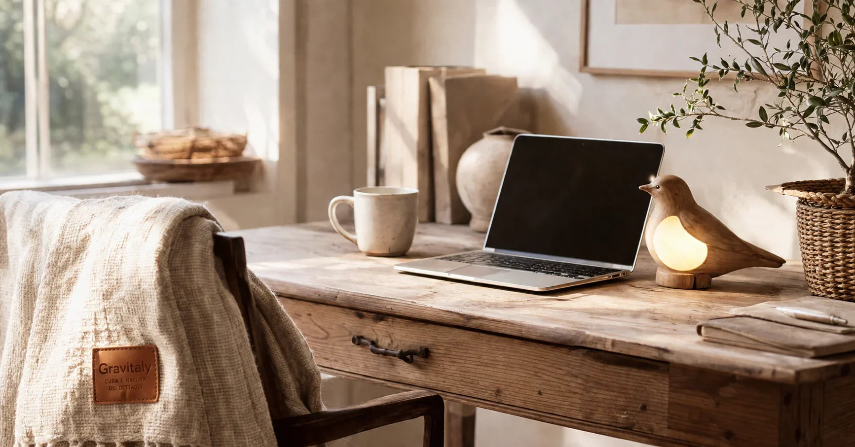 Oficina en casa acogedora con escritorio de madera rústica, taza de cerámica, portátil, manta de punto, lámpara con forma de pájaro y decoración de mimbre