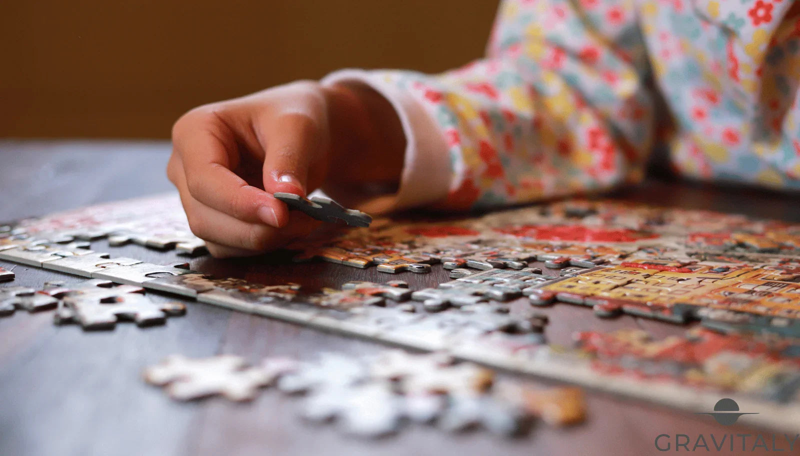 Kind setzt buntes Puzzle auf einem Holztisch zusammen, florales Langarmshirt sichtbar