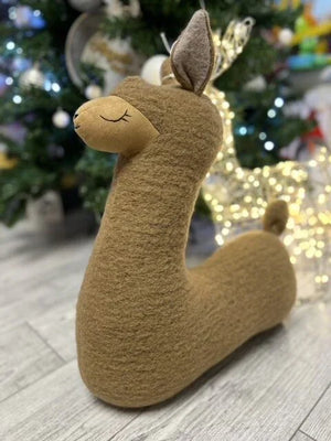 Tan felt alpaca plush toy with closed eyes, soft texture, festive background