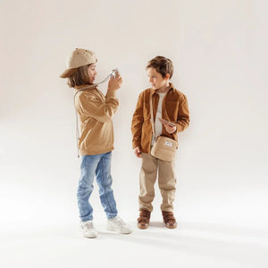 Enfants jouant avec un appareil photo « Hoppstar Artist Memo » beige et un jeu de mémoire, tenues décontractées, fond neutre