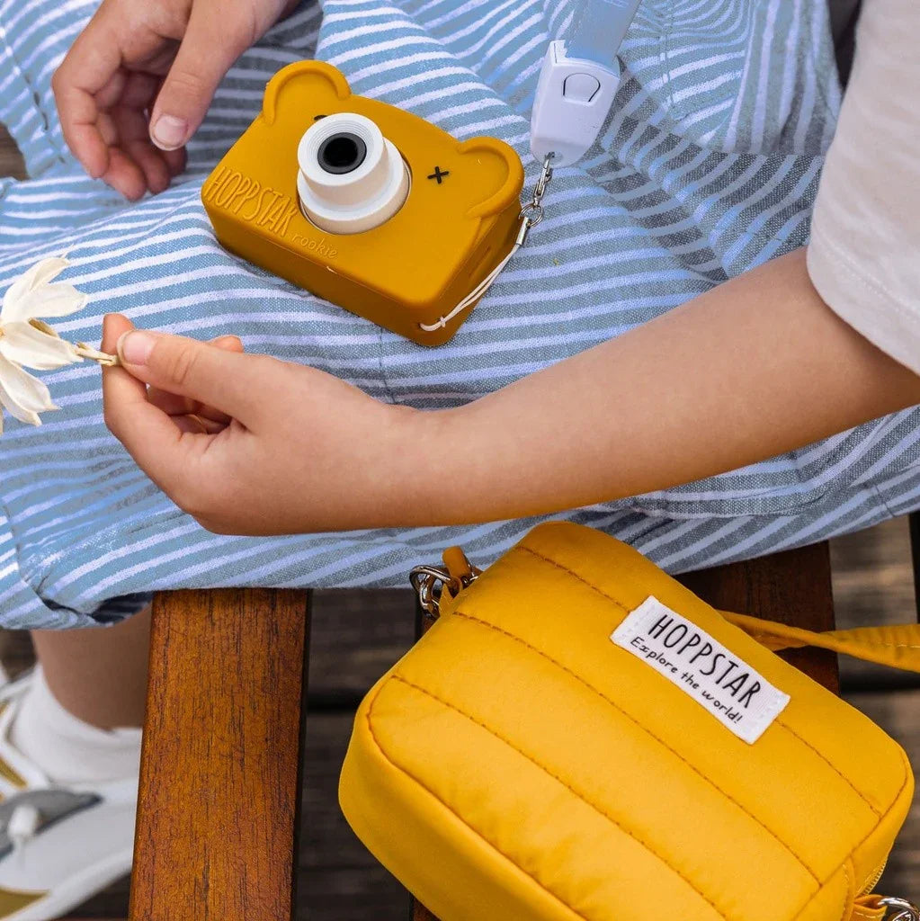 Mini borsa fotografica Hoppstar gialla e fotocamera per bambini a forma di orsetto con tracolla in tessuto sulle ginocchia di un bambino