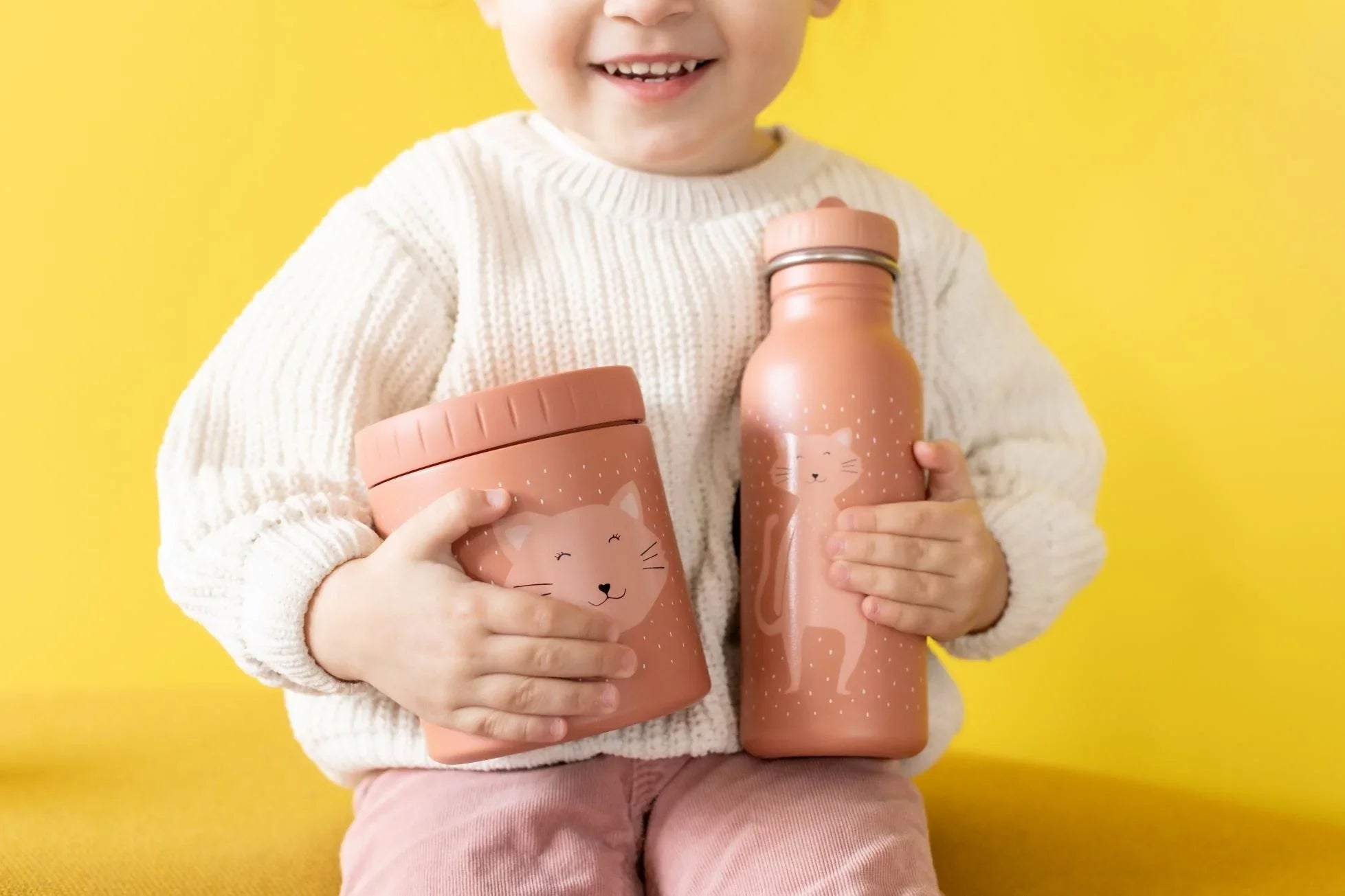 Niño sujetando un recipiente térmico rosa y botella con diseño de gato, acabado mate, patrón divertido