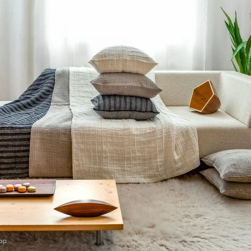 Neutrale und graue Leinenkissen und Bettwäsche, gestapelt auf einem modernen Sofa in einem gemütlichen Wohnzimmer