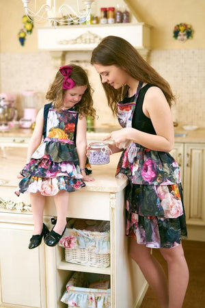 Mother and daughter in matching floral aprons baking in kitchen, child wears pink bow