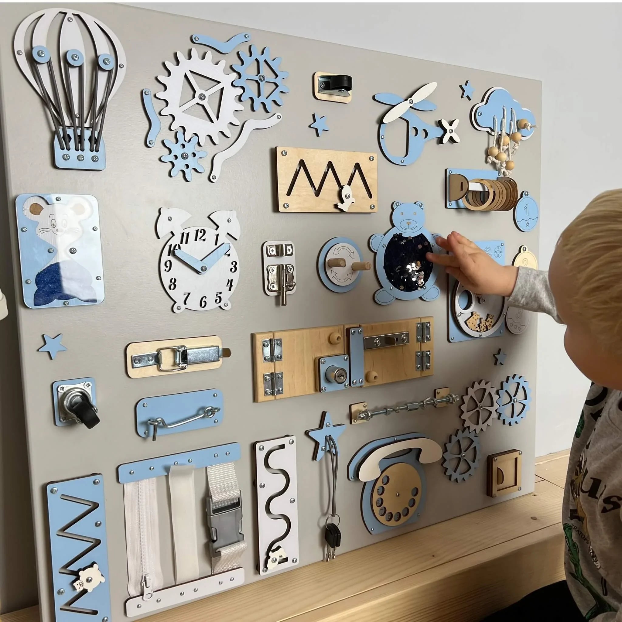 Blue and white wooden toddler activity board with gears, latches, clock, and sensory toys for nursery development