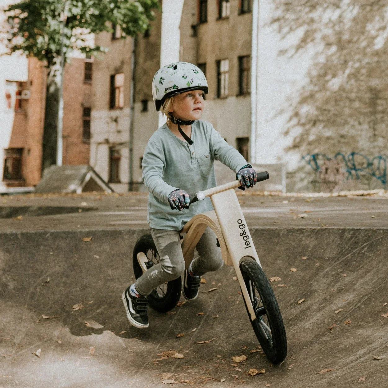 Child riding wooden balance bike with black tires and 'leg&go' branding in urban park