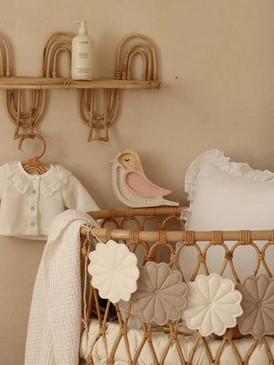 Rattan nursery shelf with wooden bird decor, flower wall hangings, and baby cardigan on hanger