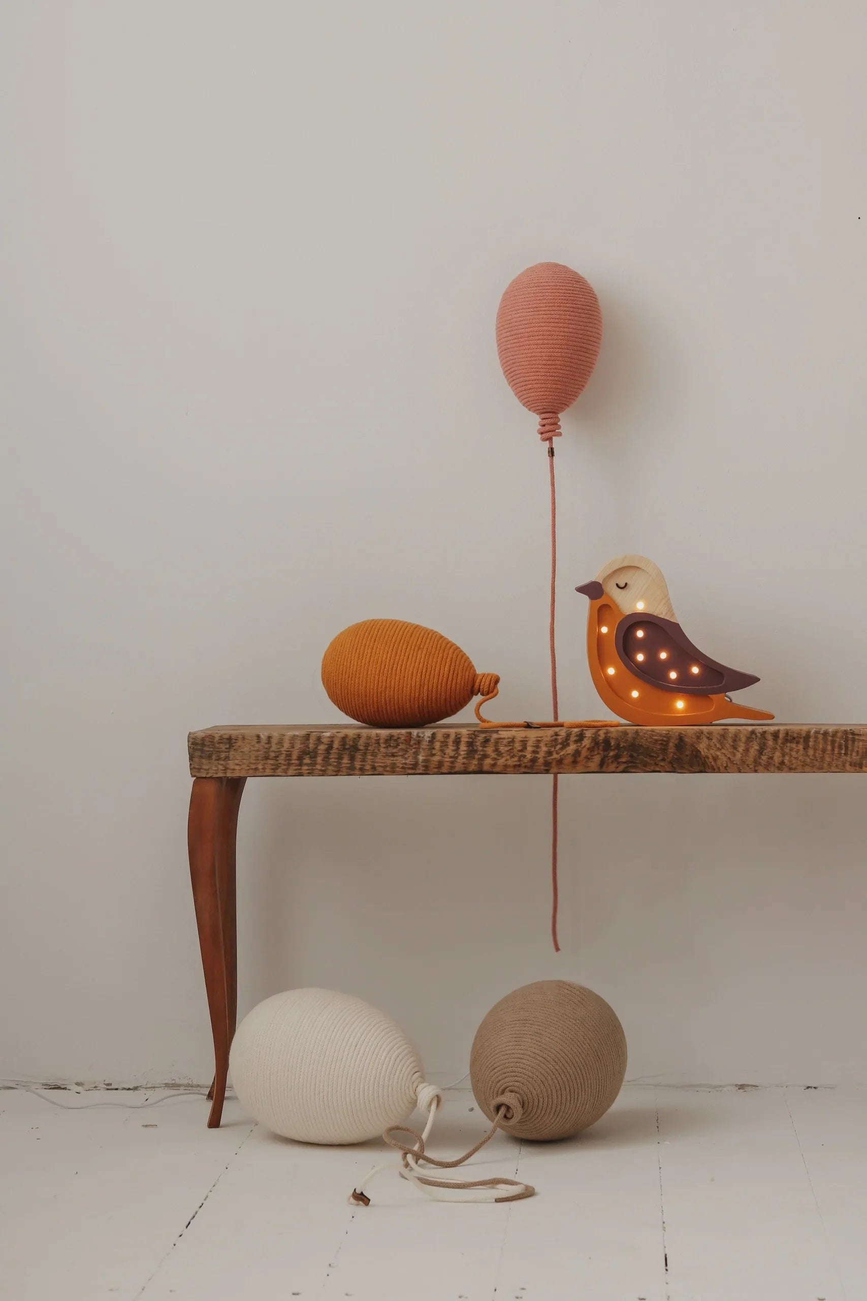 Wooden bird night light with warm LEDs, paired with hand-knitted yarn balloon decor in terracotta, mustard, cream, and beige tones.