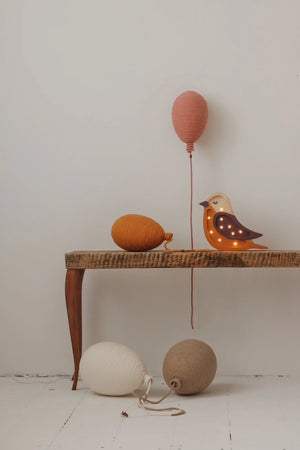 Wooden bird night light with warm LEDs, paired with hand-knitted yarn balloon decor in terracotta, mustard, cream, and beige tones.
