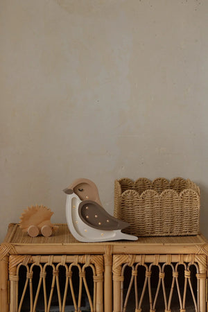Wooden bird night light with warm LED dots, natural finish, on rattan shelf beside hedgehog toy
