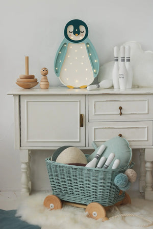 Wooden penguin night light with fairy lights, mint wicker toy cart, and wooden stacking toys on white dresser