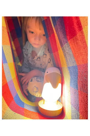 Niño con luz nocturna de pájaro de madera y altavoz bajo una manta de cuadros colorida