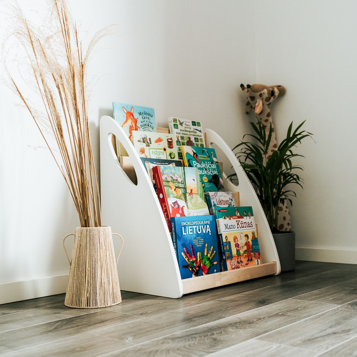 Angled Montessori bookshelf filled with children’s books beside a woven vase and indoor plant