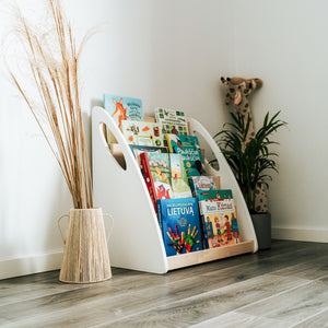 Angled Montessori bookshelf filled with children’s books beside a woven vase and indoor plant