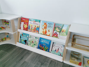Two-shelf front-facing Montessori bookcase positioned between curved and straight modular storage units